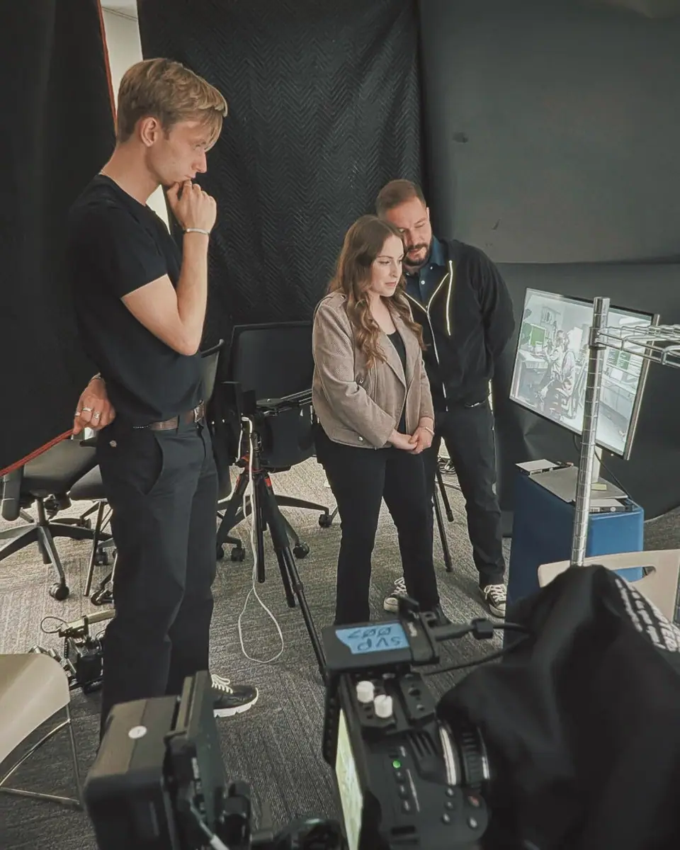 A director and two clients reviewing a take on set, surrounded by monitors and a camera rig