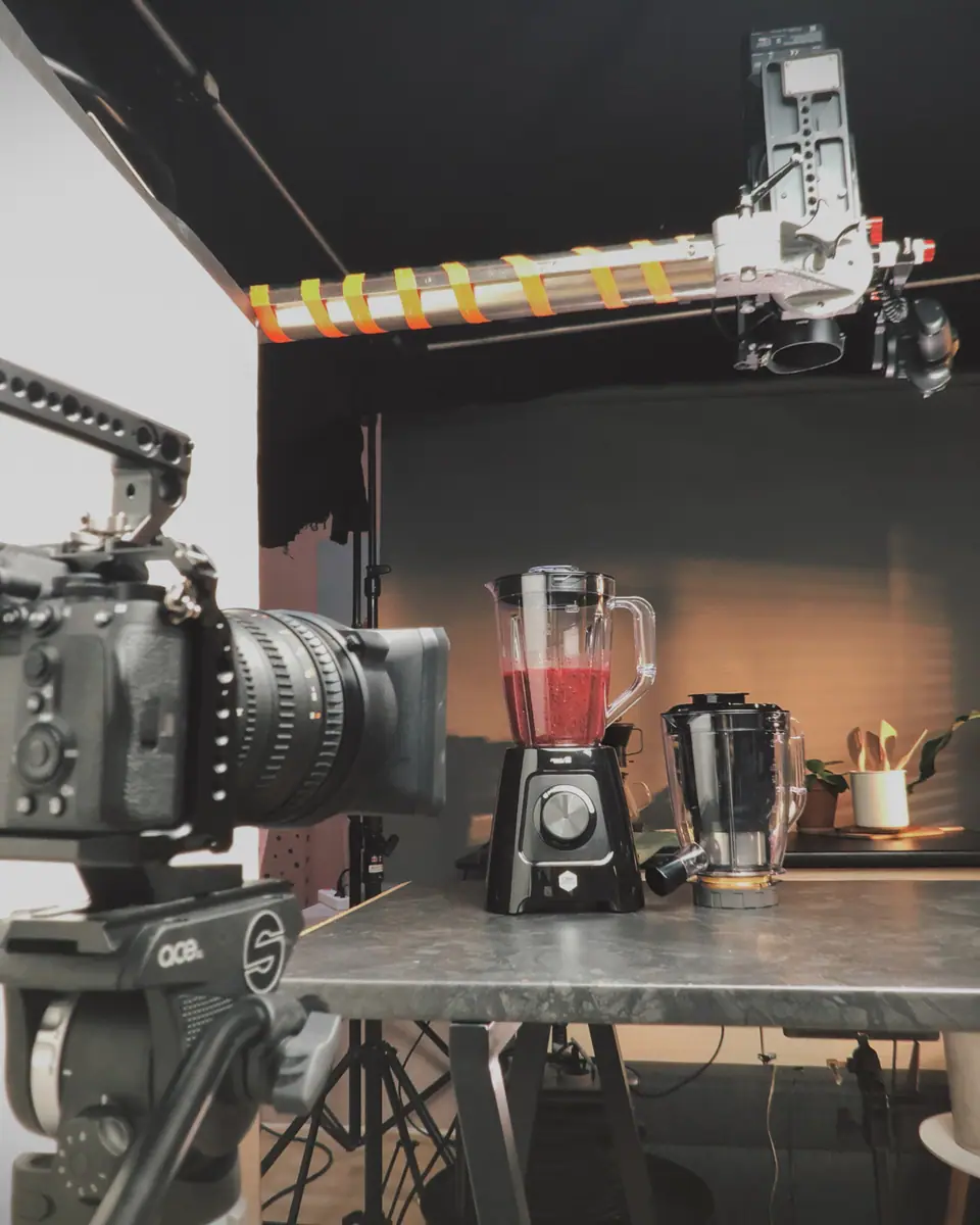 A cinema camera on a slider framing a blender with a red smoothie on a kitchen counter