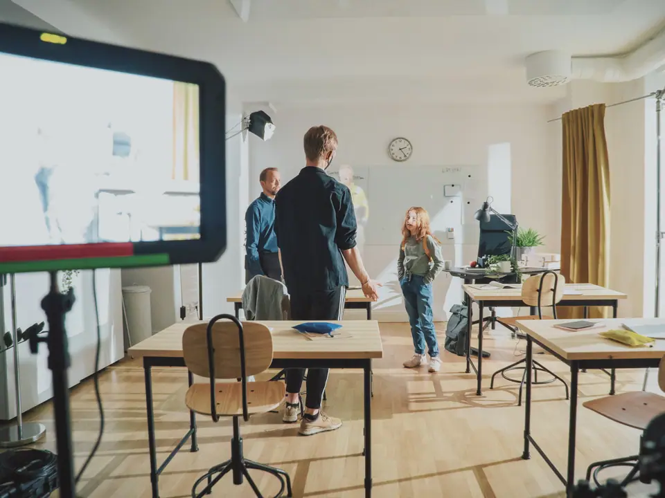 A classroom set with a child and crew, seen past a large monitor