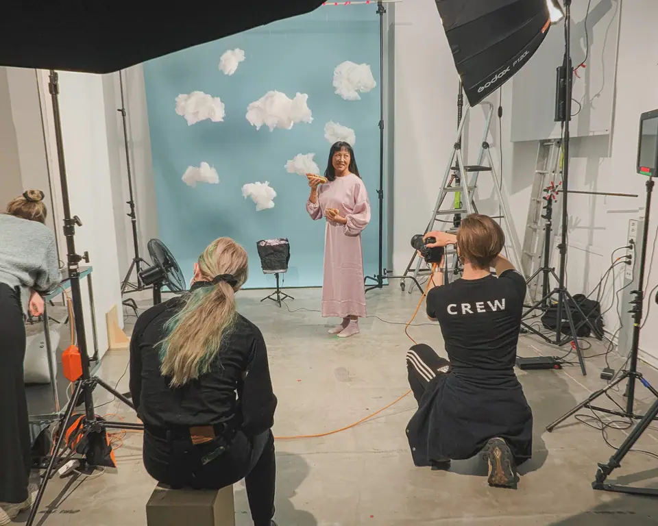 A photographer and crew shooting a woman in a pink dress against a blue backdrop with paper clouds