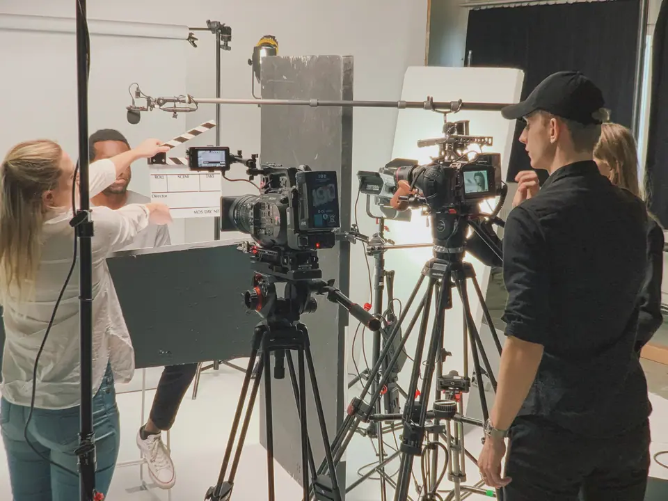 Two cinema cameras on tripods with crew and a clapperboard on a studio set