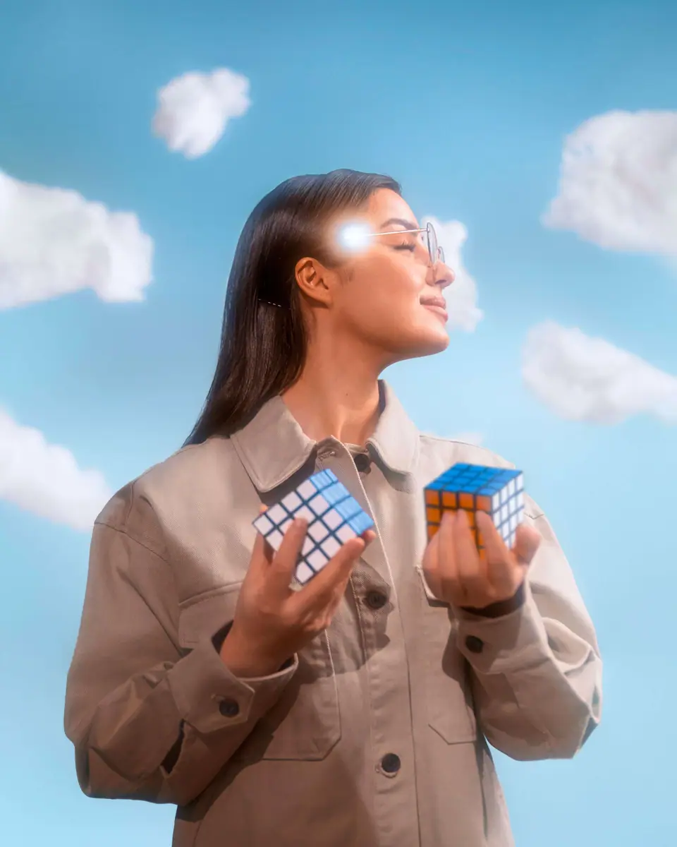 A woman against a blue sky holding two identical Rubik's cubes, one copy-pasted