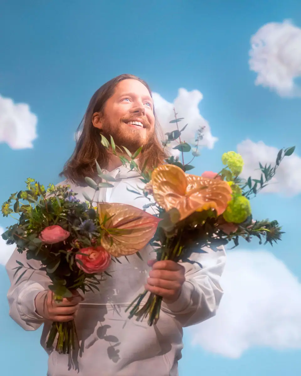 A laughing man against a blue sky holding two identical bouquets, one copy-pasted