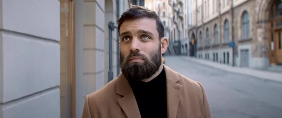 A bearded man in a camel coat on a Stockholm street