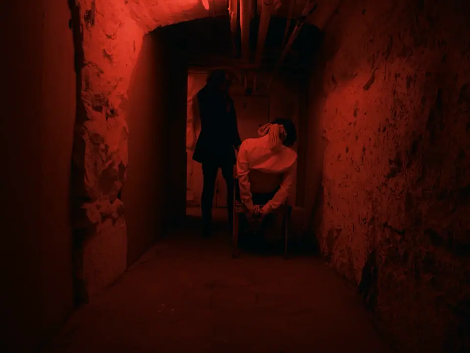 Two figures in a narrow corridor bathed in red light