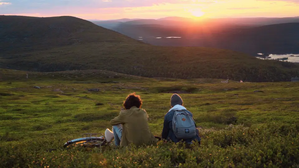 Two teenagers resting on a hillside under the midnight sun
