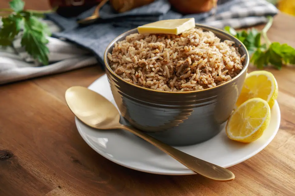 Mbahal, a spiced rice dish, served in a dark bowl with lemon wedges and a gold spoon