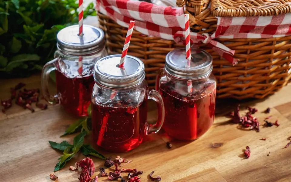 Deep-red hibiscus drinks in mason jars with striped straws, beside a picnic basket