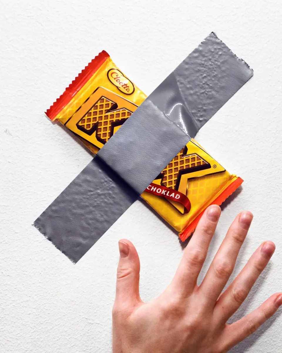 A Cloetta Kexchoklad bar duct-taped to a white wall, a hand reaching up for it