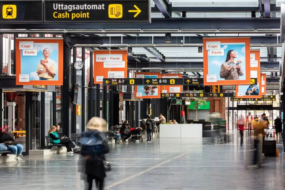 Copy/Paste campaign banners hanging over a station concourse, travellers walking below