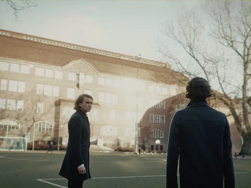 Two men in long coats facing each other in a schoolyard