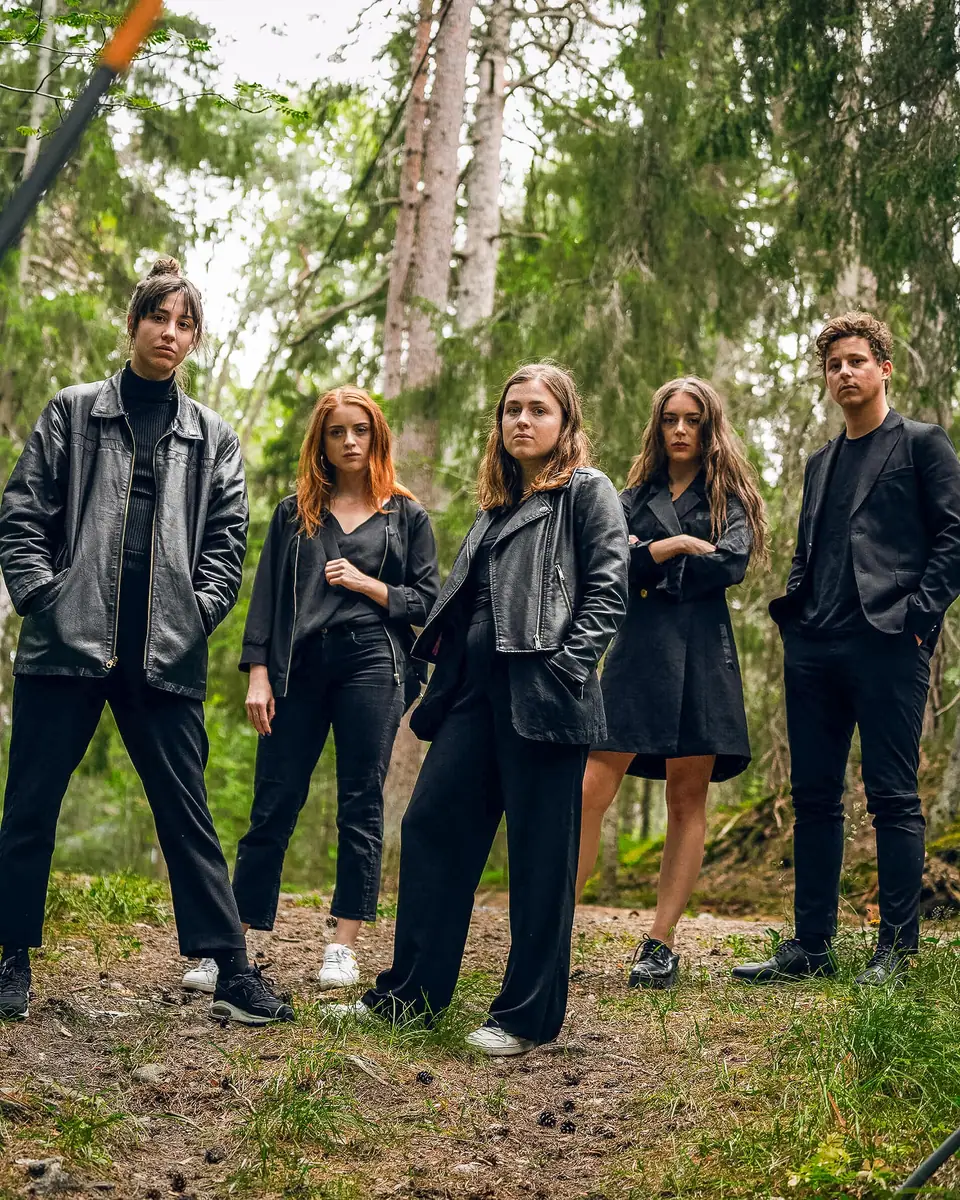 Five young people dressed in black standing together in a pine forest