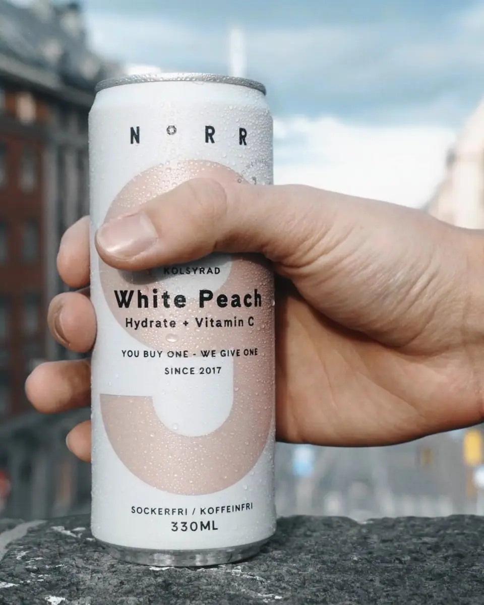 A hand holding up a can of Norr White Peach against a pale sky