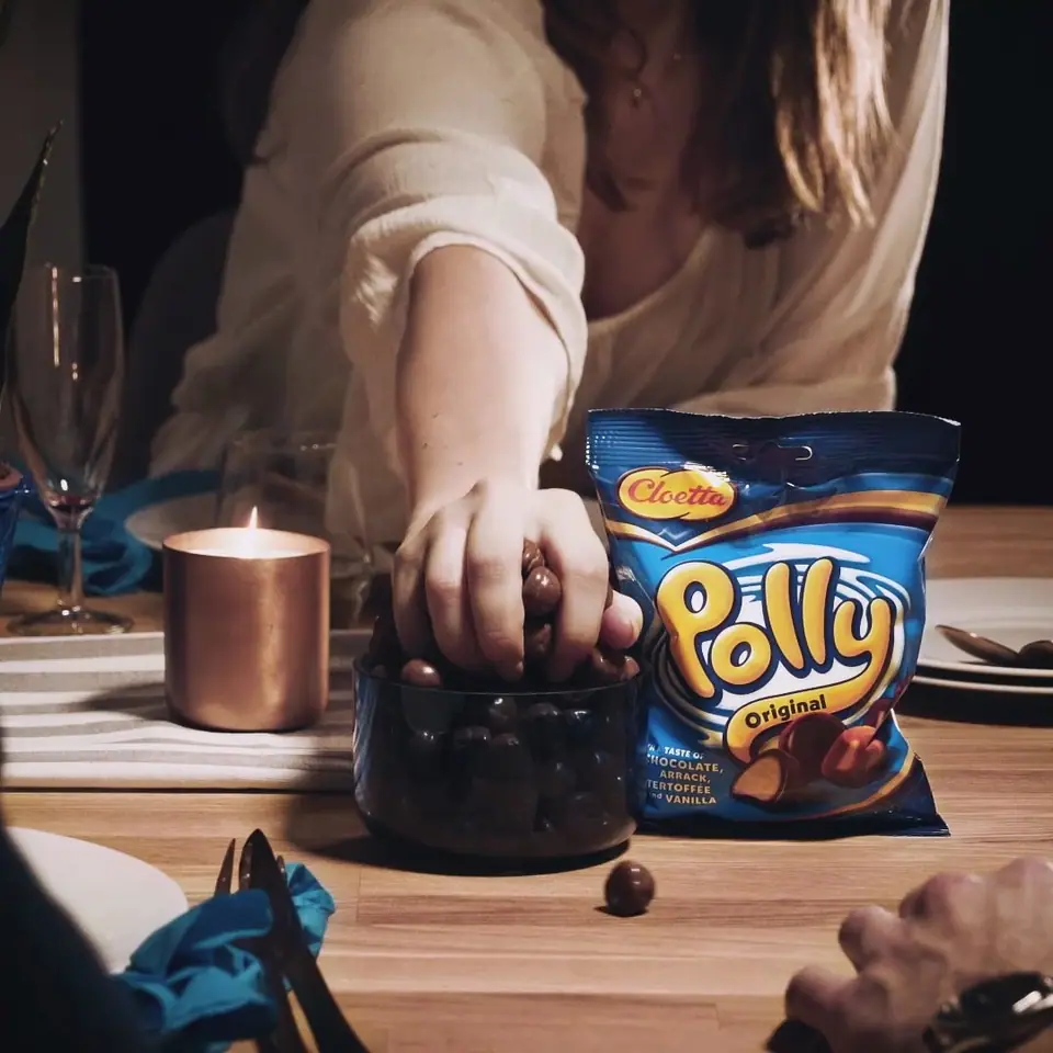A hand reaching into a bowl of Polly chocolate candy beside a candle