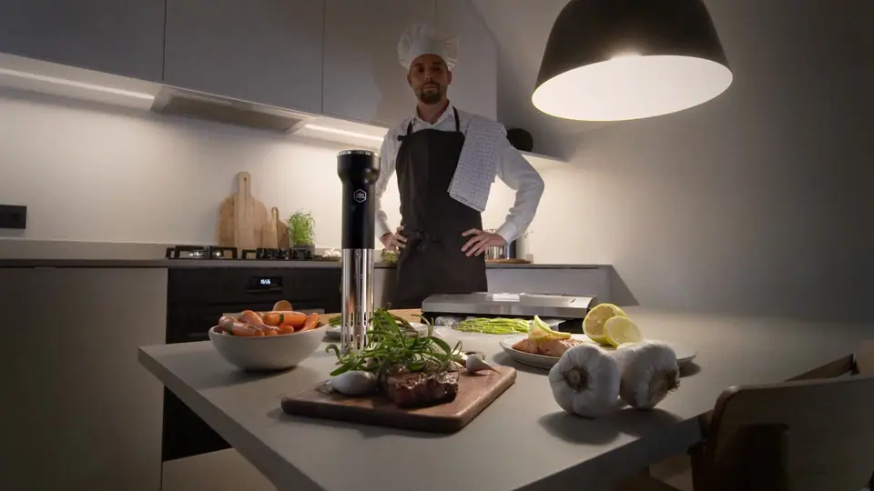 A chef in an apron standing in a kitchen behind a counter set with food