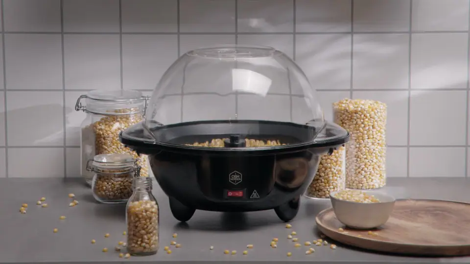 An OBH Nordica popcorn maker on a tiled kitchen counter surrounded by jars of corn