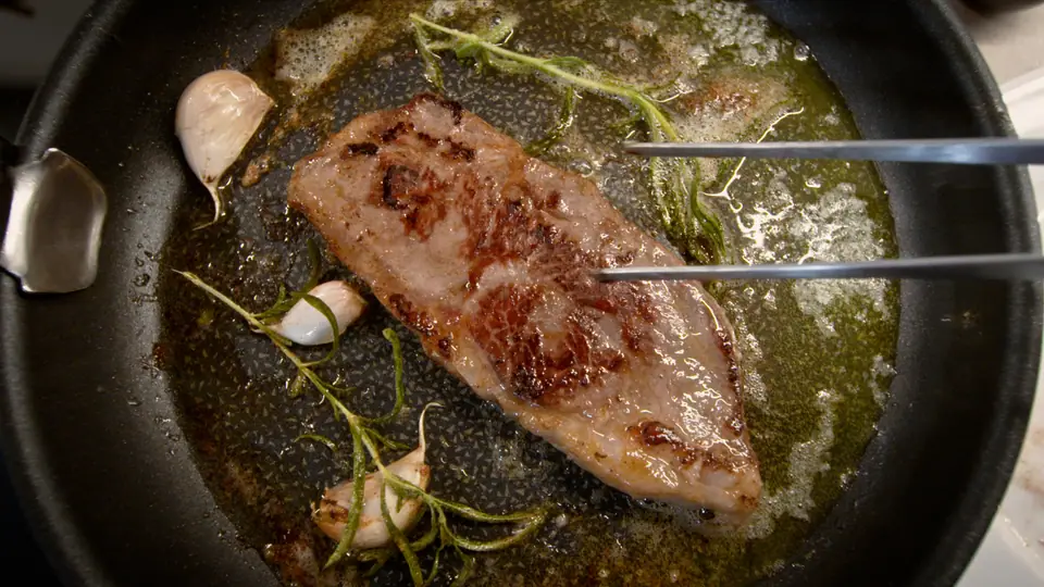 A steak searing in a pan with herbs and garlic, from the OBH Nordica Sous Vide film
