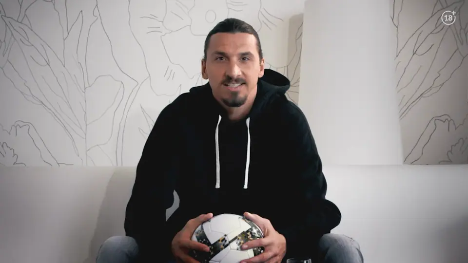 Zlatan Ibrahimović smiling on a white sofa, holding a football